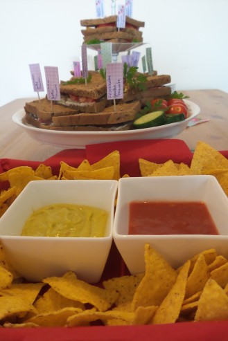Tortilla Chips mit zwei Dips. Im Hintergrund Sandwiches auf einer Etagere.